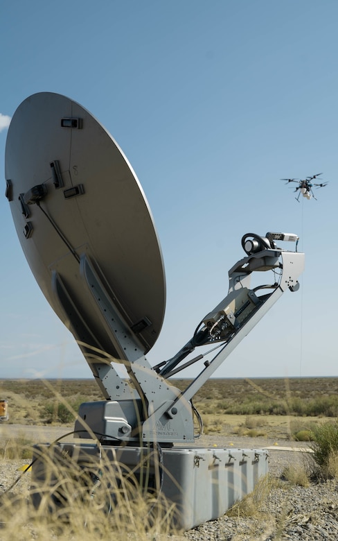 A drone flies past a satellite dish.